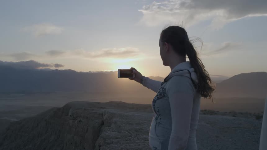 Man stands on a cliff taking a picture of nature