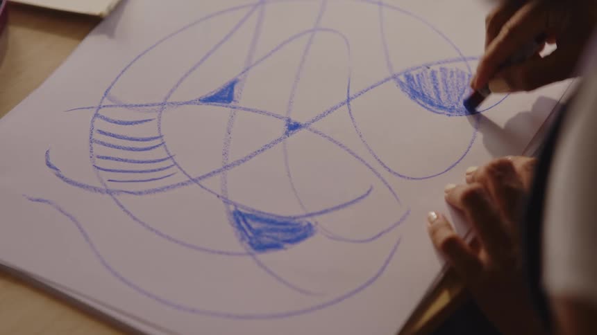 Hands with blue crayons drawing on white cardboard