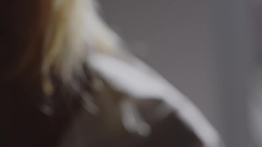 A blonde woman is stroking the hair of a person standing in front of her