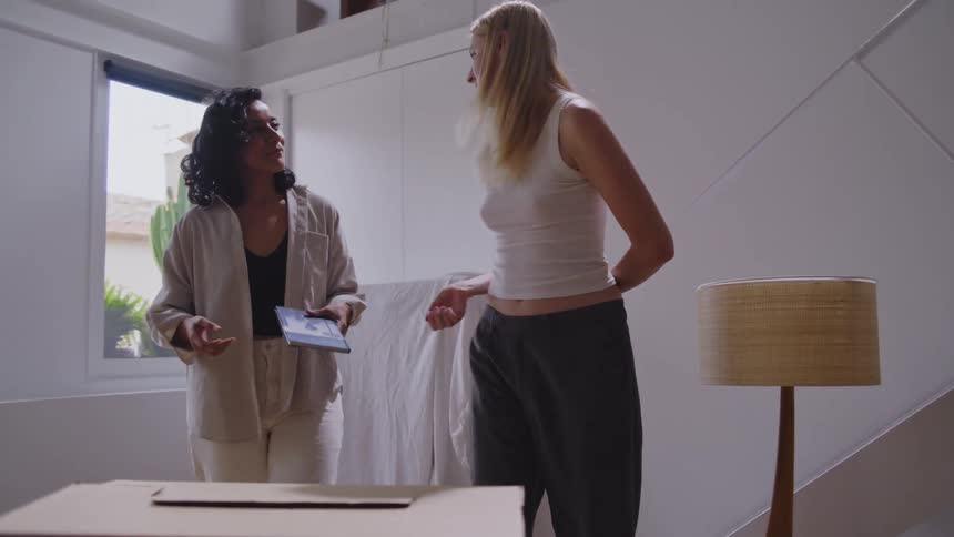 Two women in a living room with boxes talking