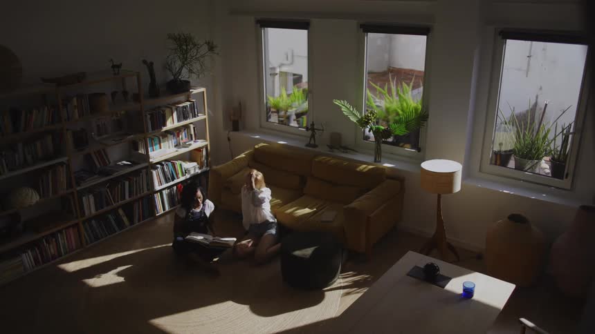 Two women sitting on the living room rug reading a book