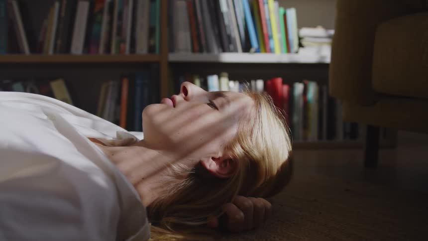 Blonde woman lying on laminate floor in living room looking thoughtful