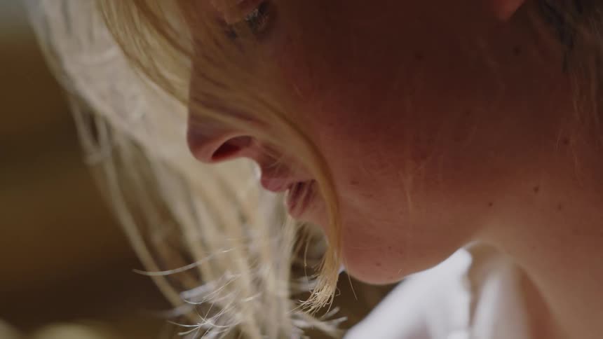 The face of a woman with blonde hair who has strands of her hair partially covering her face and she is looking down