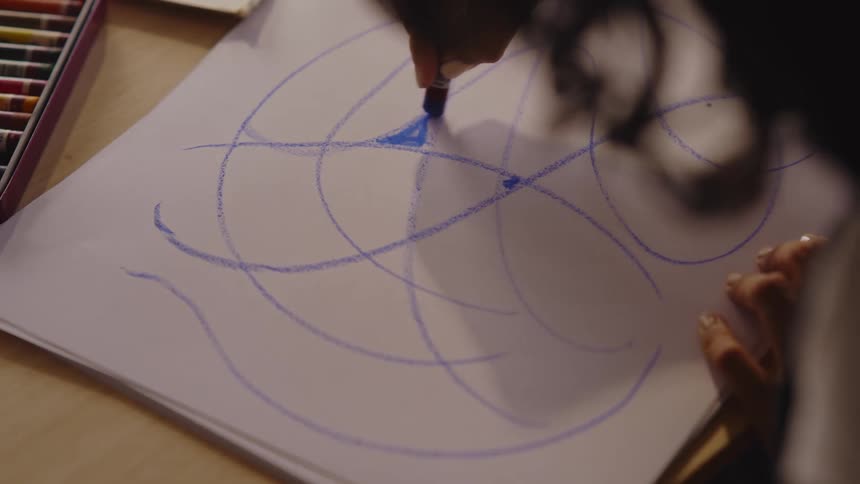 Top view of a woman drawing with crayons on a white poster board