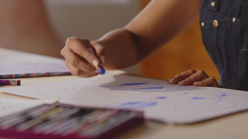 Artist sitting at a table adds blue to a drawing on a large sheet of paper