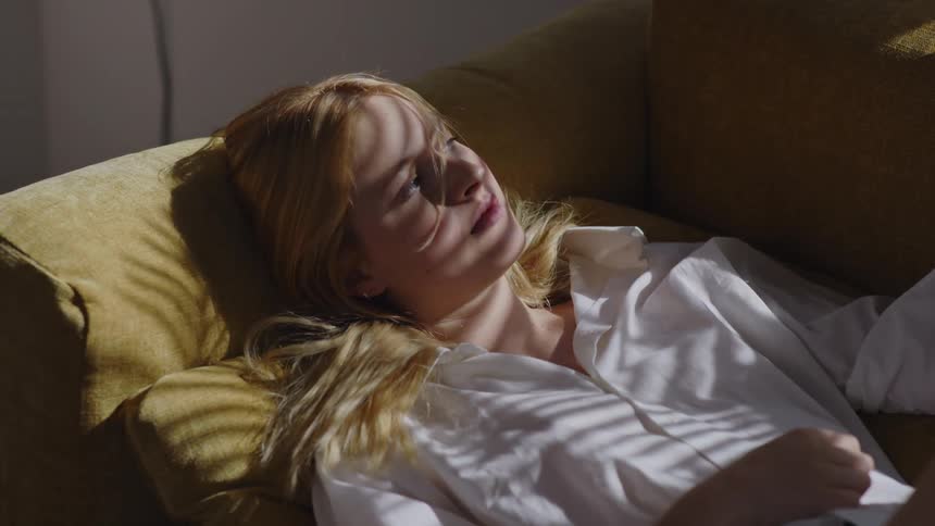 Blonde woman with a white shirt lies down on a yellow couch