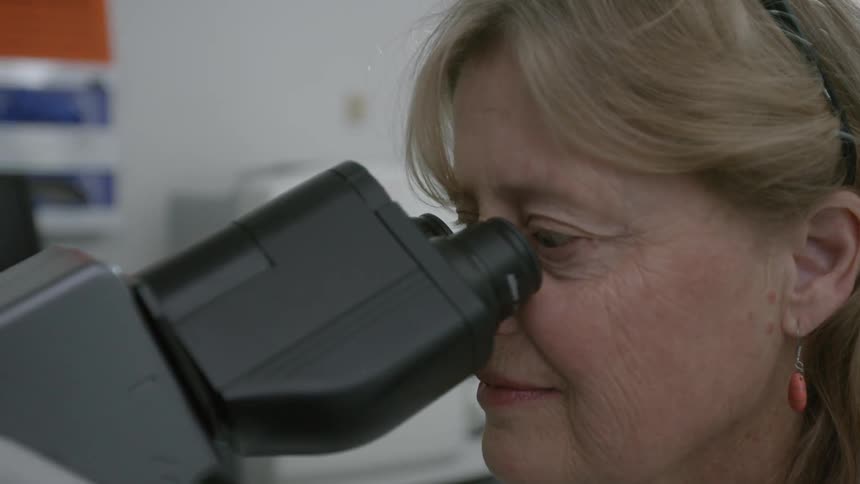 Elderly woman looking into a microscope