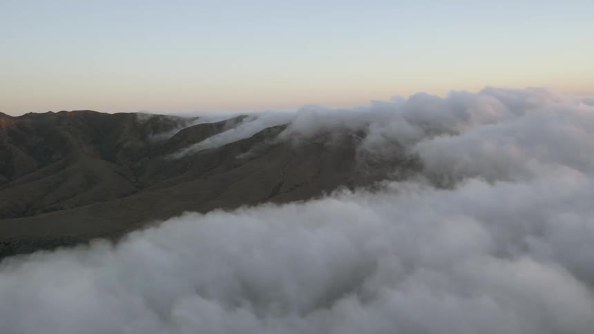 Clouds are rolling over a mountainside at dusk
