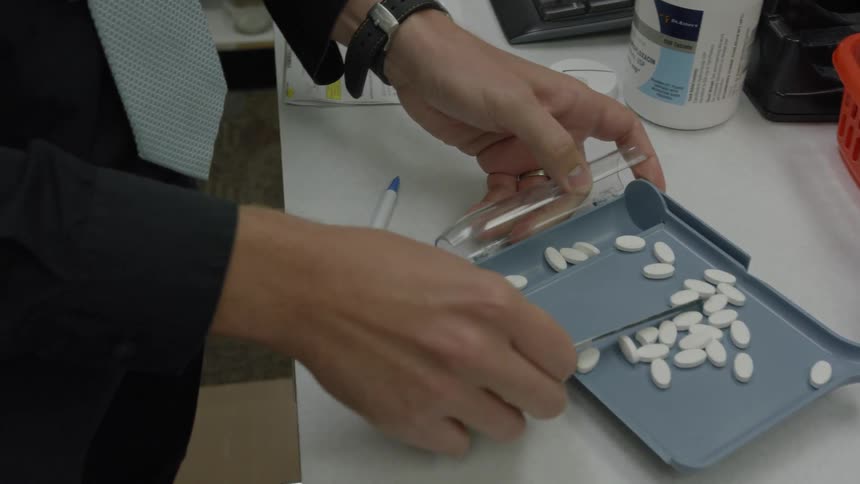 A pharmacist is scraping pills into a tube
