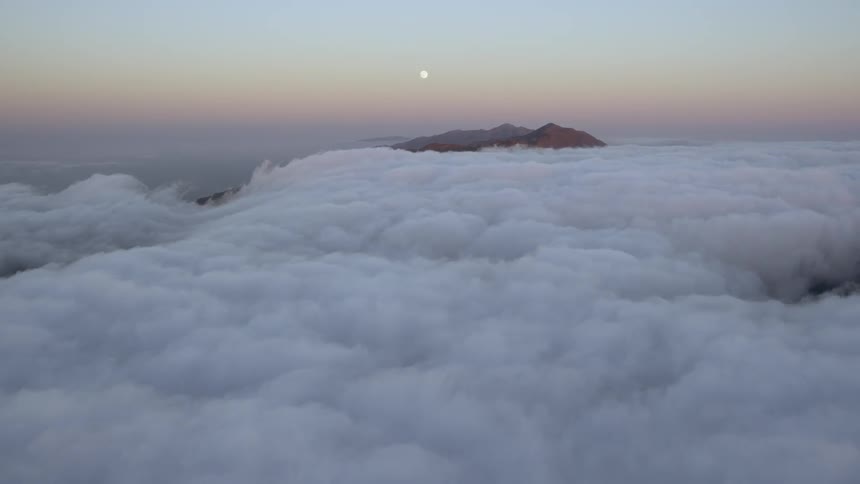 Clouds are rolling across a mountain range at dusk
