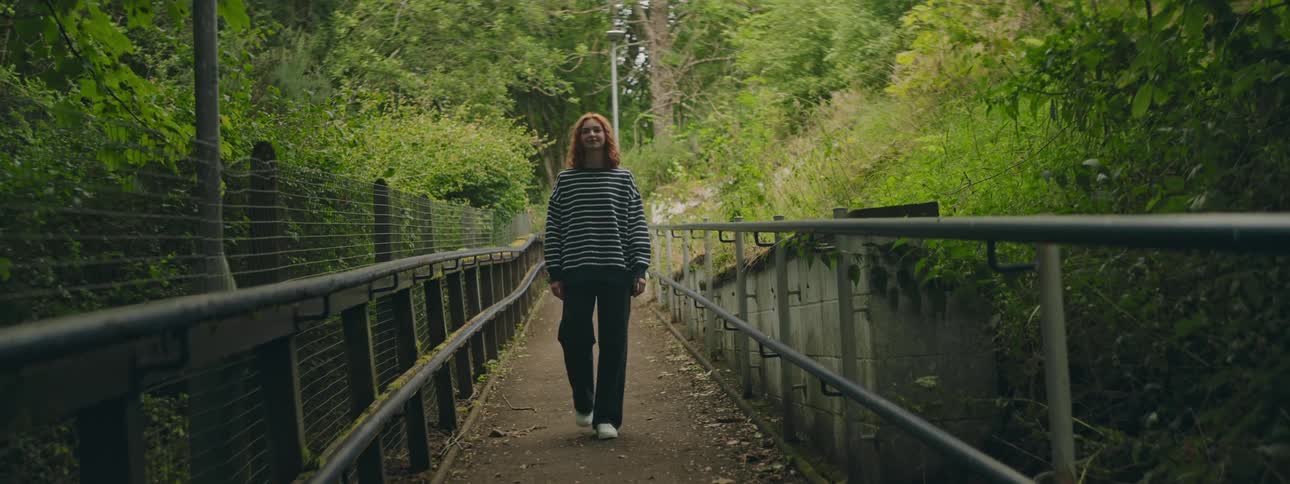 Redhead woman walking a way in a park surrounded by trees