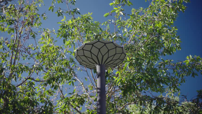 Metal lamp post topped with a geometrical metal framework stands among the trees under a blue sky