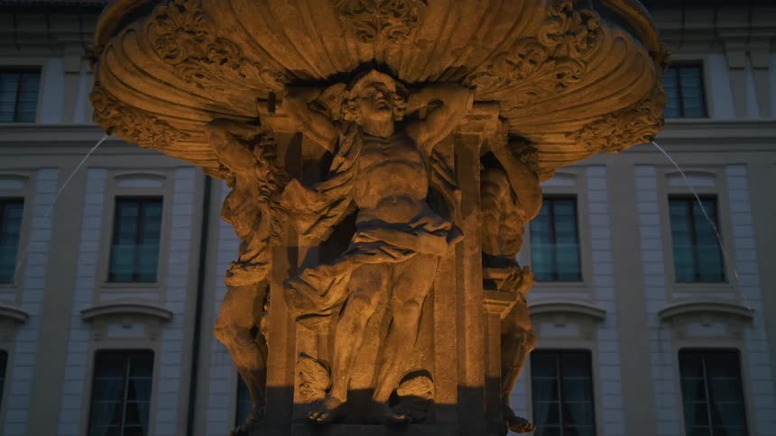 An illuminated ornate fountain adorned with sculptured figures with water reflections