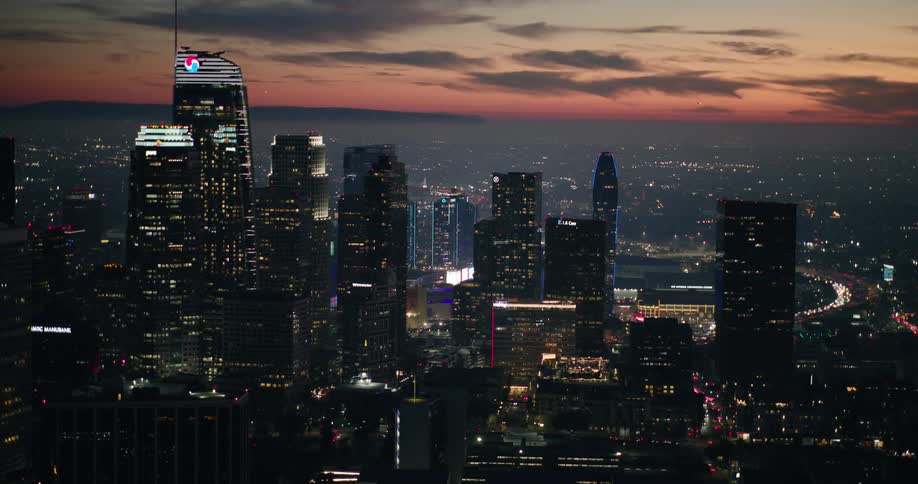 An aerial shot of the los angeles skyline at dusk showcasing illuminated skyscrapers and city lights