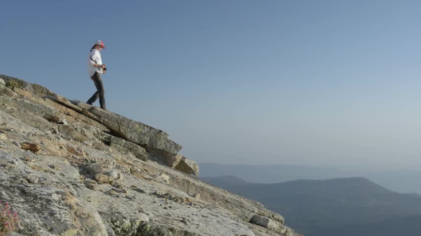 Person walking down and standing very close to the edge of a mountain top on a clear day