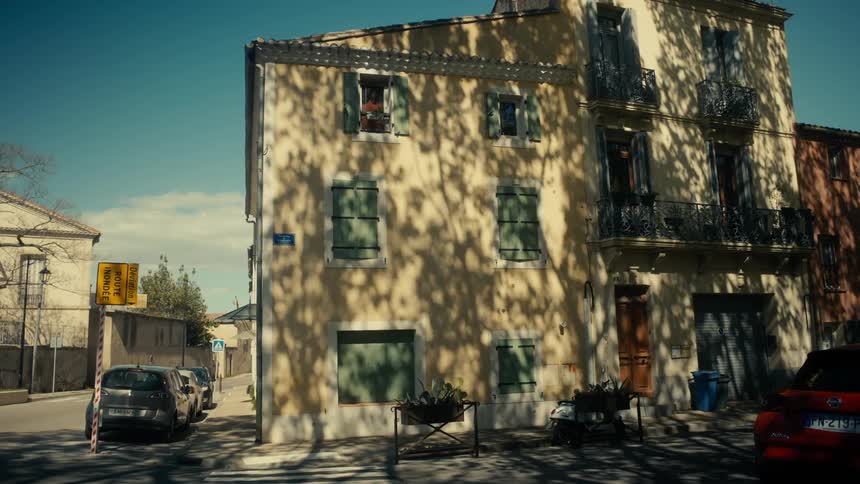 A white car drives past a three story home sitting on a street corner