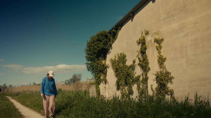 A person walks along a dirt path beside an ivycovered building stopping to take a picture