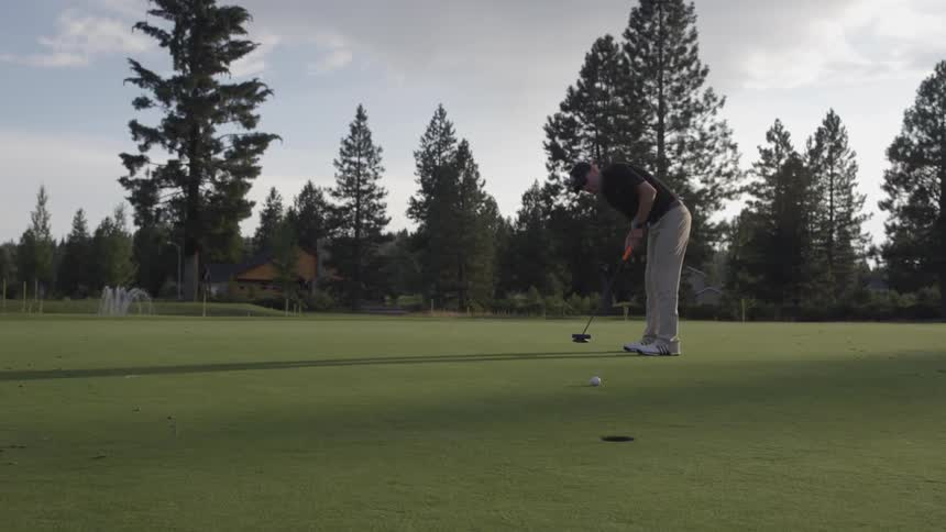 Golfer making a successful medium-range putt on a mostly cloudy day