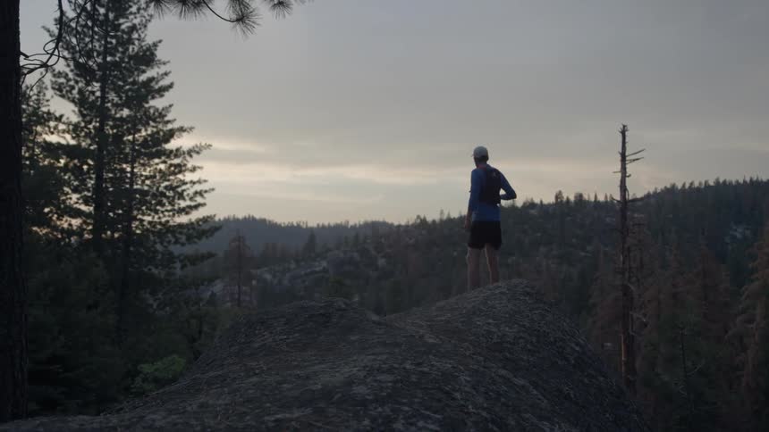 A man jogs onto a ridge in a natural setting then stops to take in the view
