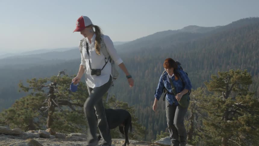 Two women with a dog walking up a mountain