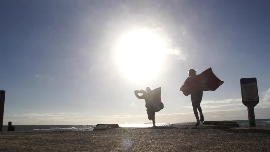 Children run with blankets towards the ocean