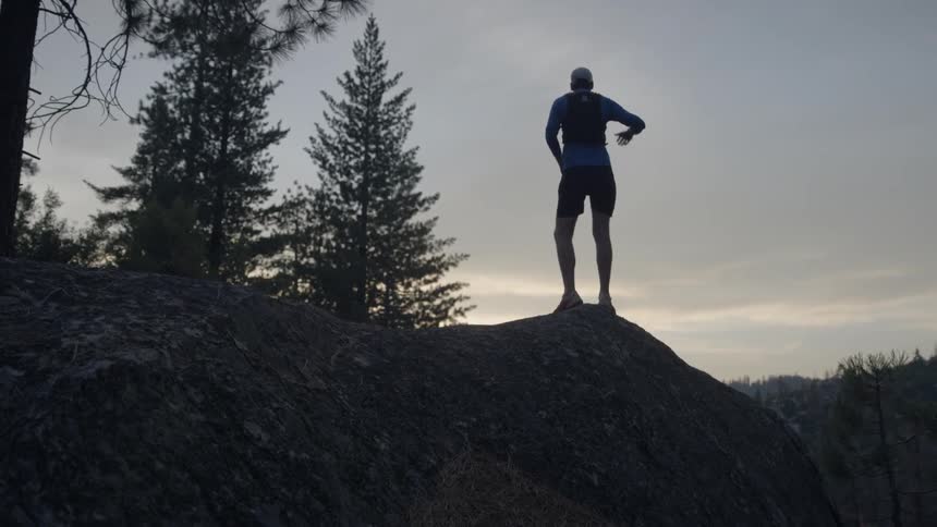 A man jogs up onto a ridge and peers into the distance at dusk
