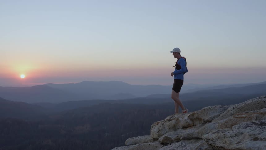 Man standing high atop a rocky mountain as the sun sets in the distance