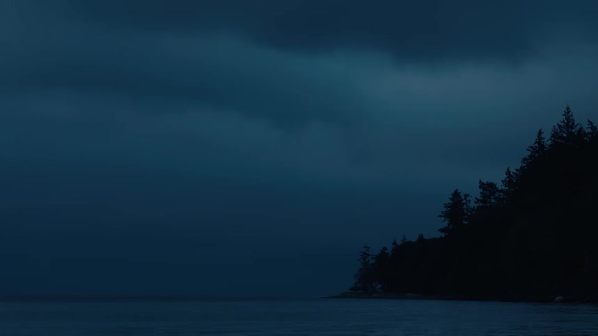 Heavy cloud cover dims the sunlight on a conifer covered coastal mountain