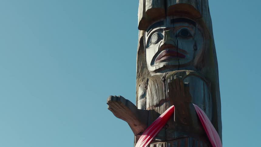 A weathered totem pole with a carved face and outstretched hand stands tall against a clear blue sky
