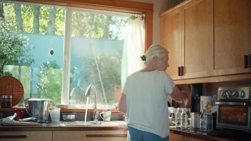 An elderly woman does the chores in the kitchen