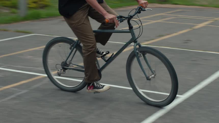A person rides a bicycle on a paved path wearing brown pants and black shoes with white soles