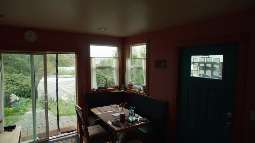 A dining table in a corner in a house interior where there is a blue door on the right side and an external glass door on the left side