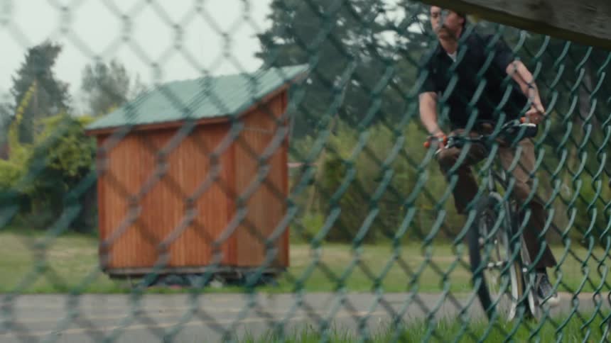 A teenager rides a bicycle around a fenced in court