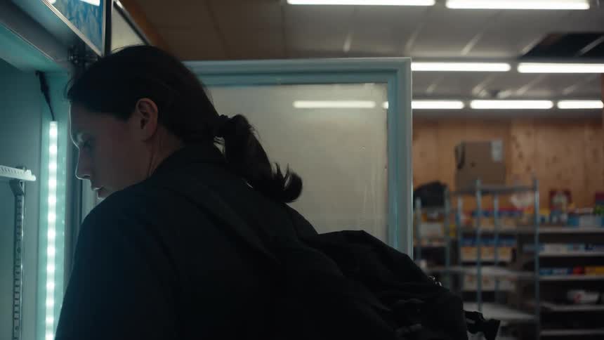 A person with long hair tied back opens a refrigerator door in a store