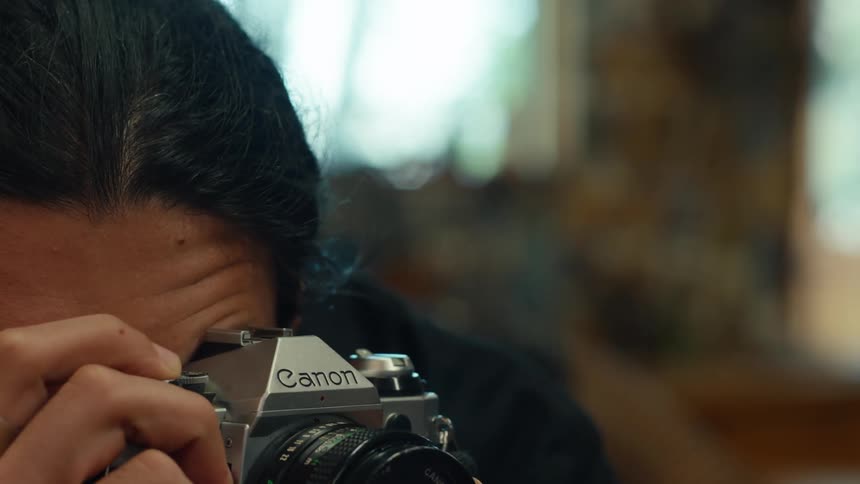 A person with a digital camera in front of their face and they are pointing forward and then they press the button with their finger to take the picture