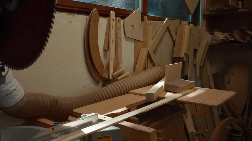 A machine inside a room and there is a table that has some wooden objects and there are other wooden objects leaning against the wall next to it