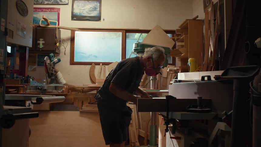 An elderly man wearing a protective mask is carrying out work with a tool that is releasing dustlike material upwards