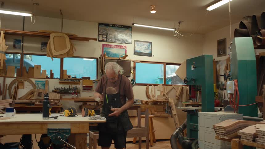 Two old men in a workshop are doing carpentry work using power tools to work on wooden objects