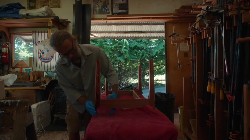 Carpenter applying varnish to the wood of a table support