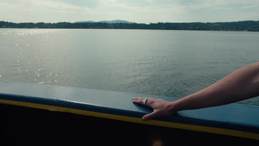 A man on a boat with his hand on the edge of the hull while the boat sails on a body of water