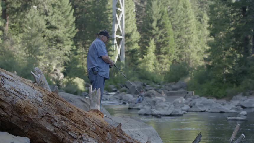 An older man is fishing in a river during the day