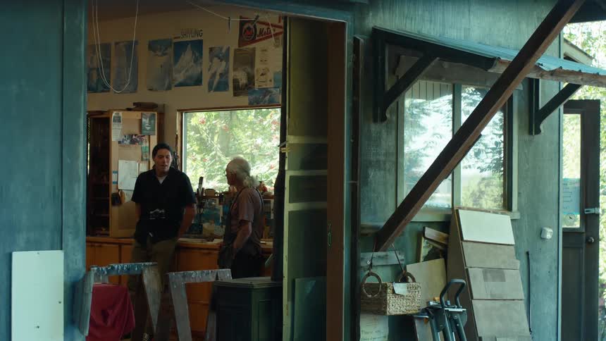 Two people stand in a cluttered workshop conversing