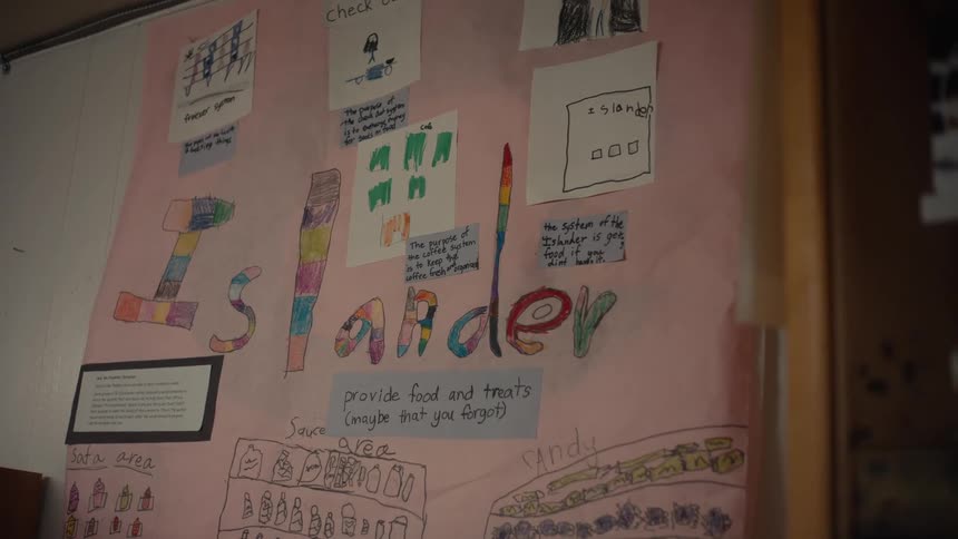 A large poster with drawings made by children is hung up on a whiteboard in a classroom
