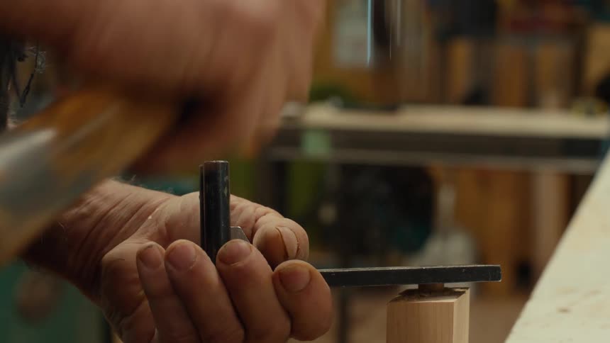 Man holding a piece of metal with one hand while hammering a pin with the other hand