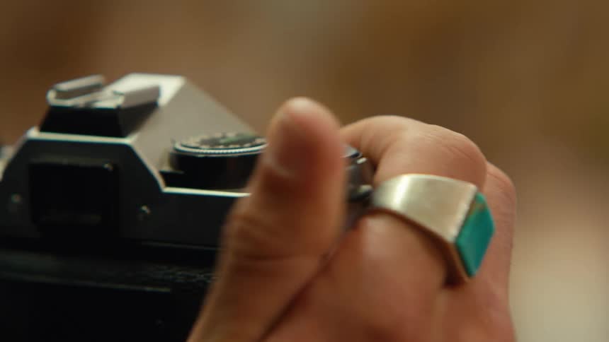 A closeup of a hand adjusting the settings on a vintage camera adorned with a silver ring featuring a turquoise stone