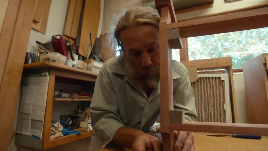 Concentrated carpenter sanding a wooden piece of furniture