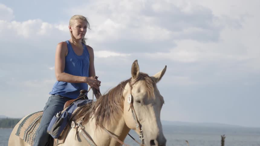 Woman rides a horse near a body of water on a cloudy day