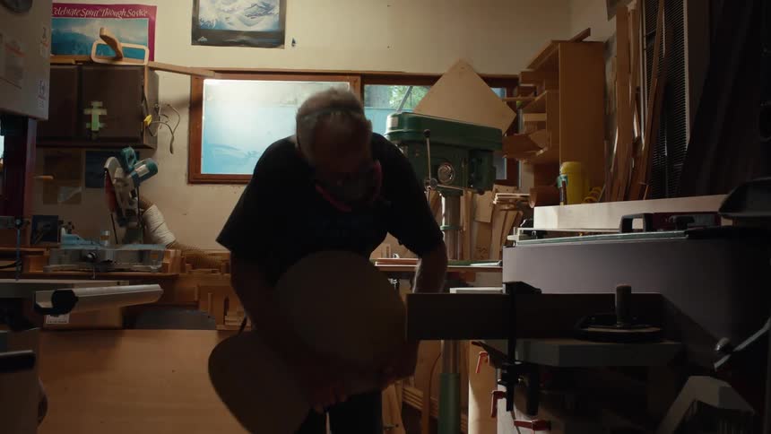 An elderly man wearing a protective mask is cutting a wooden object using a machine