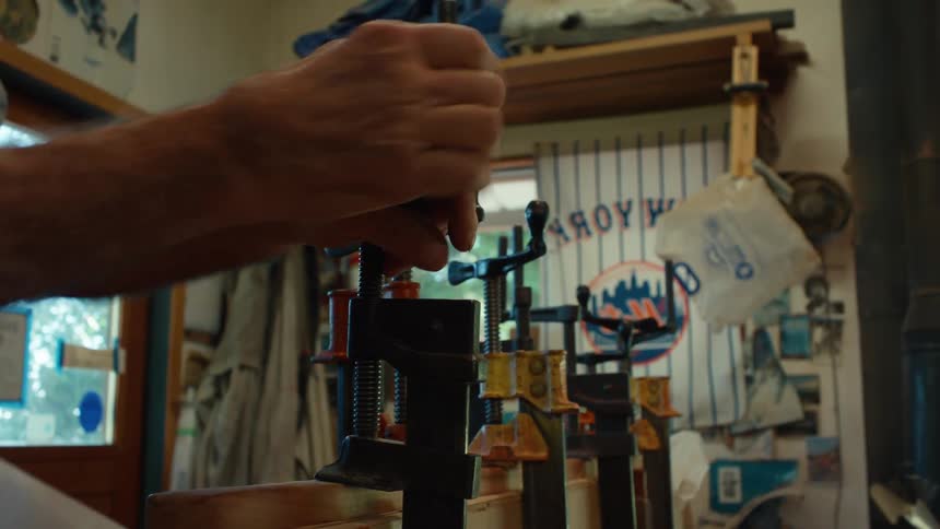 An elderly man using his hand and a pipe tool to tighten an object that is holding a wooden slat