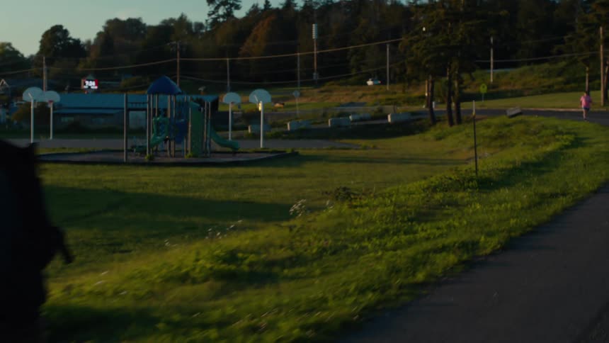A man rides past a playground with a basketball hoop and a slide which sits empty in the fading light of dusk